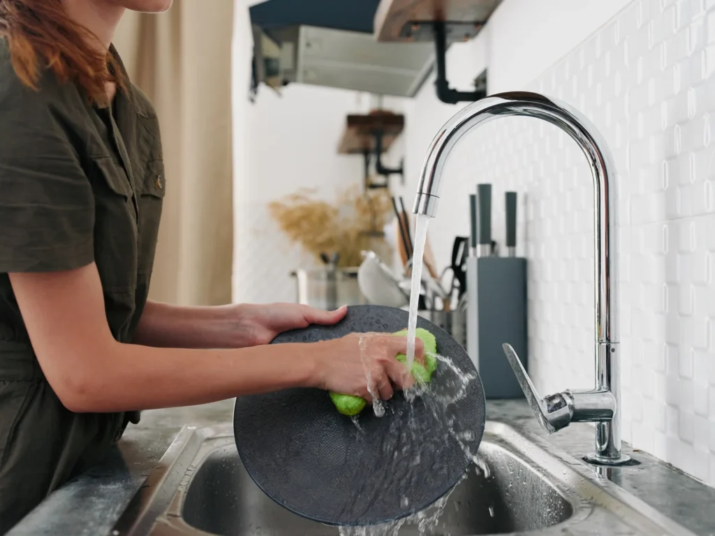 A woman washing dishes with hot water